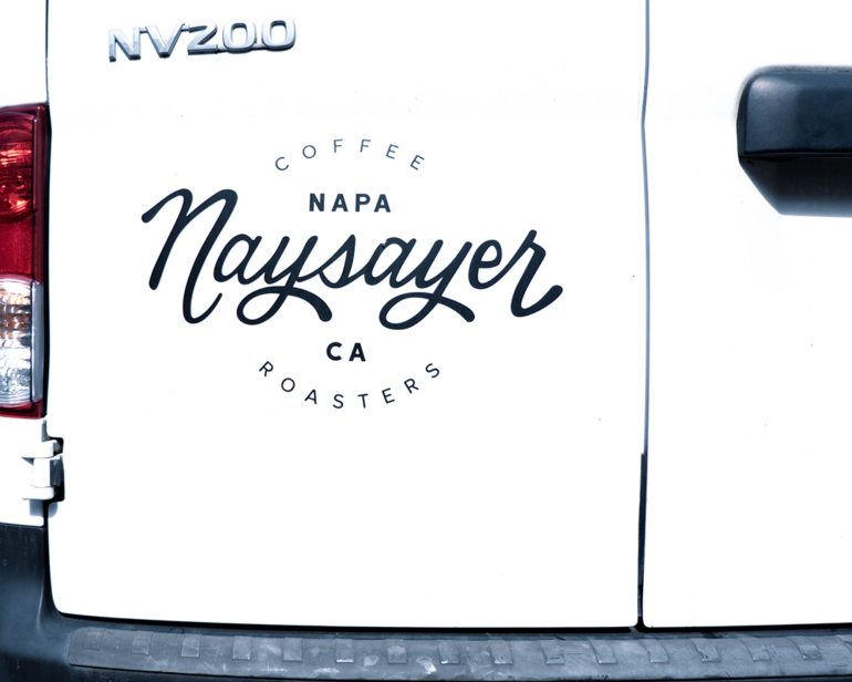 The back doors of a white delivery van with the Naysayer Coffee Roasters of Napa logo in black across the left door.