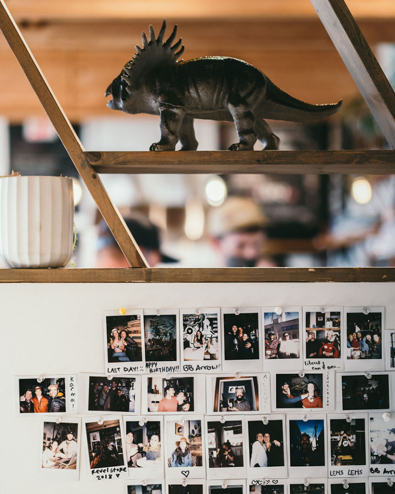 A toy triceratops on a shelf above a wall of polaroid photos of various Revelstoke regulars and Dose staff.