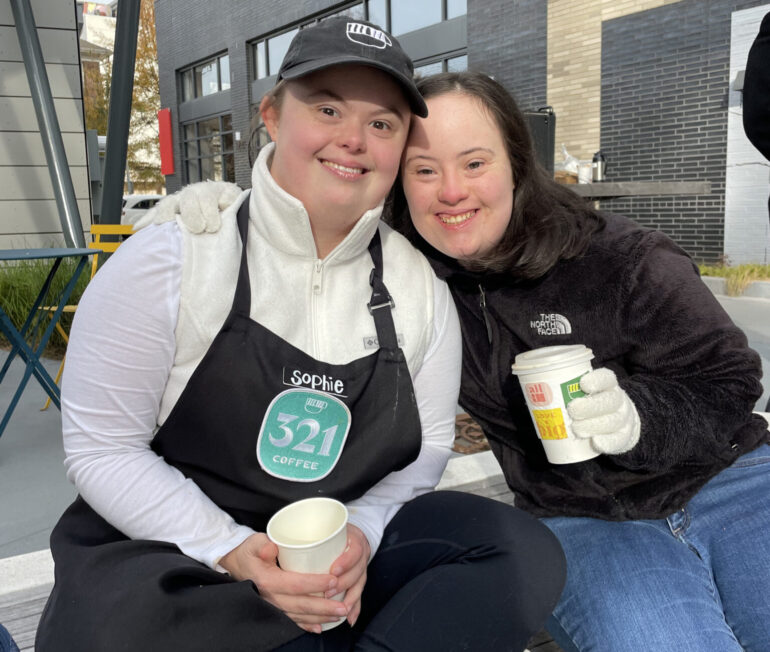 Two female employees of 321 Coffee share coffee and a hug outside the café.